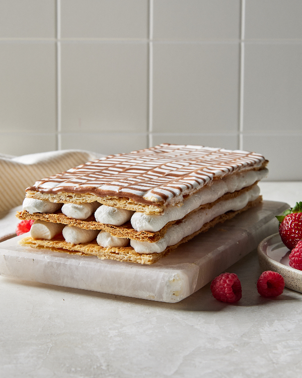 A Mille-Feuille cake on a marble slab in a kitchen with a tile backsplash, shown with loose strawberries and raspberries.