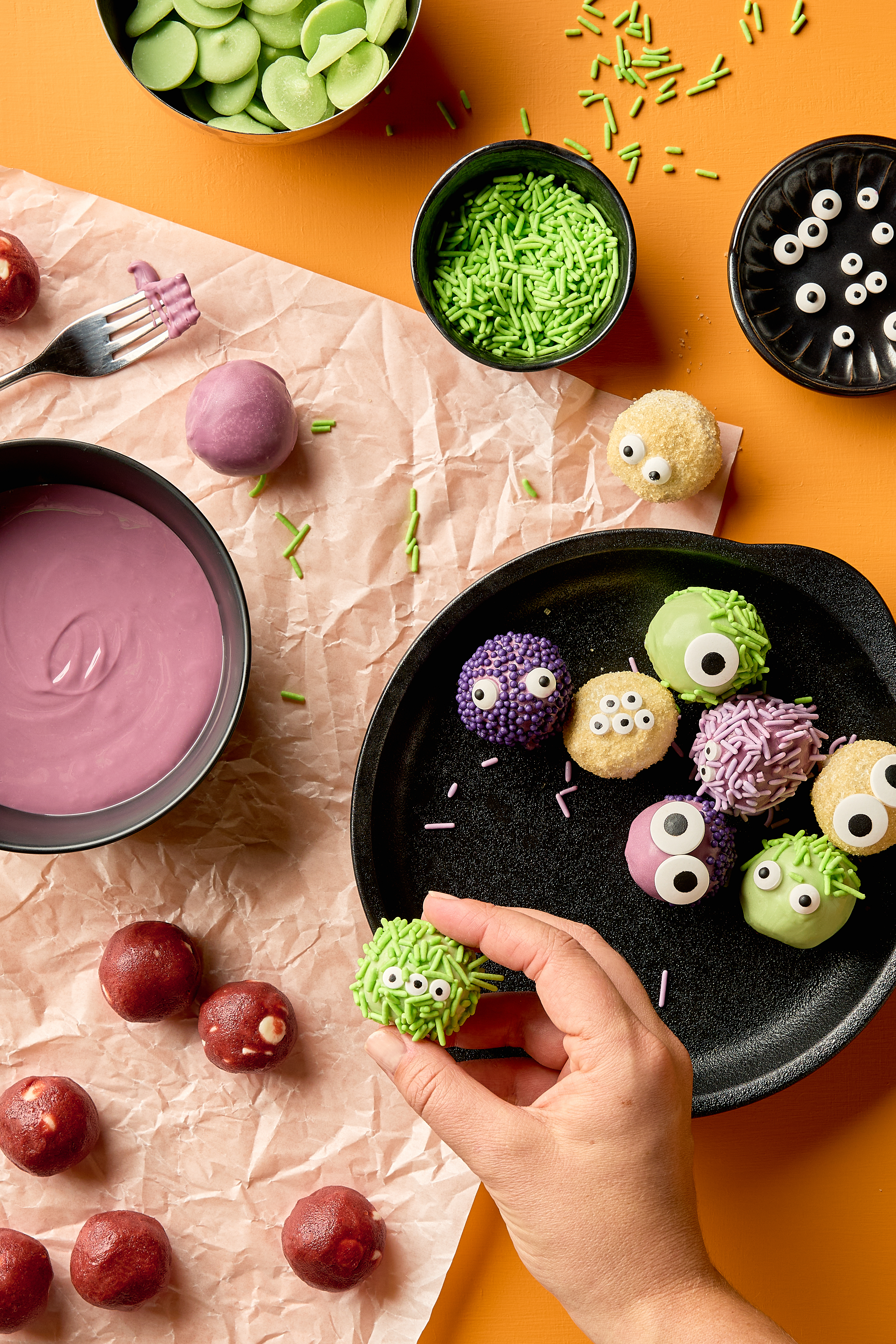 A glass bowl of red velvet cookie dough truffles dipped in white chocolate with drizzle. One is shown cut in half, with the red centre visible.