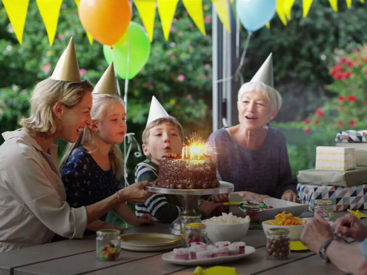 Group gathered around a table at a birthday party as a child blows out candles on a cake