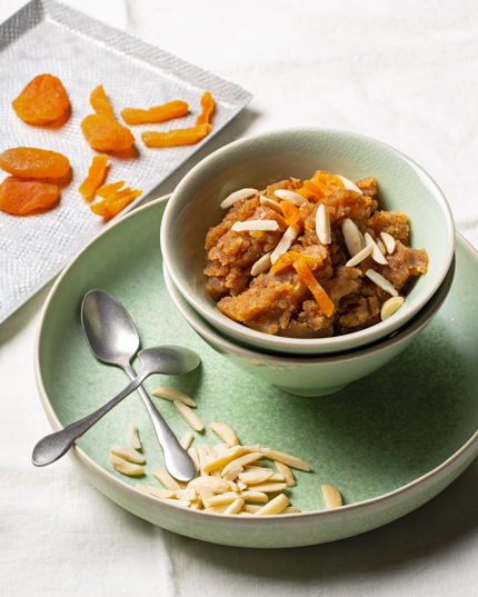 Bowl of whole wheat halwa on a green platter with a spoon and sliced almonds