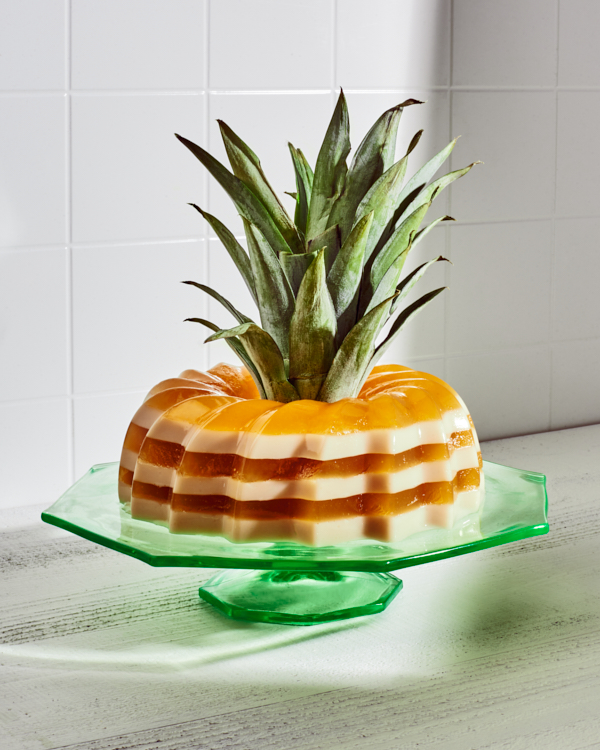 Piña Colada Layered Gelatin Dessert on a green glass stand shown decorated with a pineapple top in the middle