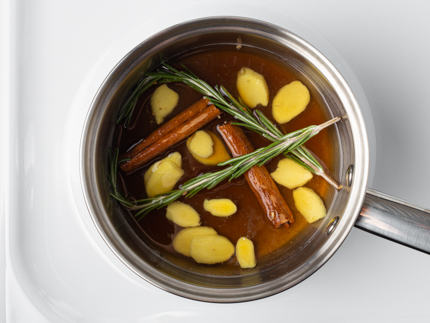 A pot of simple syrup on a stove with rosemary, ginger, and cinnamon sticks