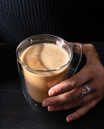 A woman’s hands holding a glass mug of Malaysian coffee with tea on a black table