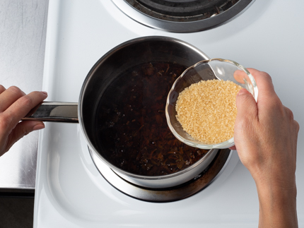 Pouring turbinado sugar from a glass bowl into a pot of hot water and tea leaves