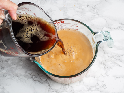 Pouring coffee from a glass measuring cup into a mixture of tea and evaporated milk