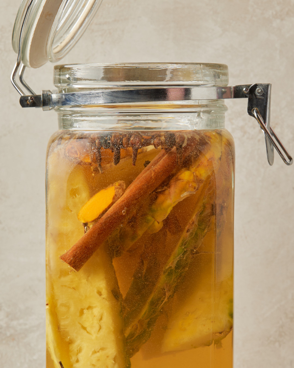 A jar of pineapple spears, cinnamon sticks, ginger, and cloves fermenting into tepache