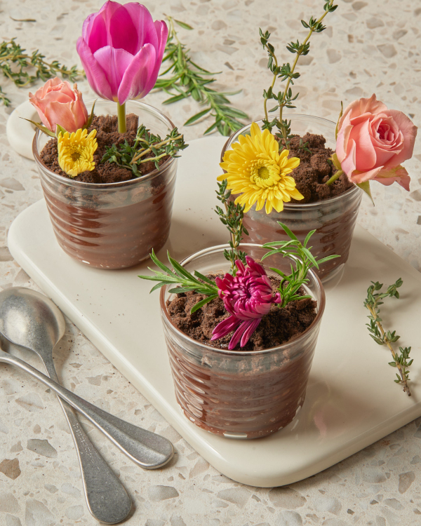 Three serviings of chocolate dirt pudding with cookie crumble topping garnished with edible flowers