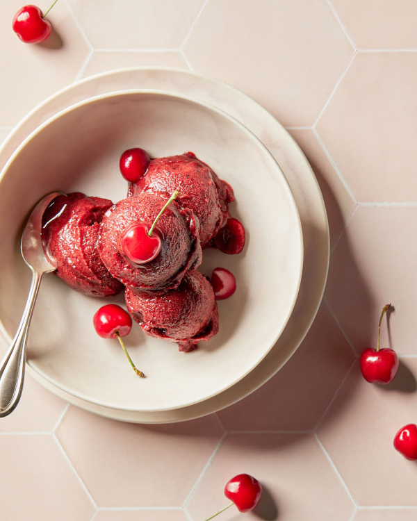 Four scoops of cherry sorbet garnished with cherries, shown on a counter of pale pink hexagonal tiles.
