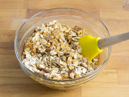 Oats, pecans, and coconut being mixed in a bowl with butter, honey, and juice