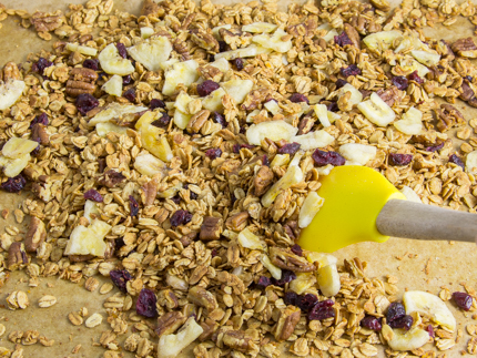 Stirring bananas and cranberries into granola on a parchment-lined baking sheet