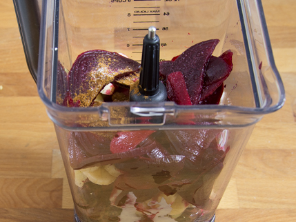 Slices of beet, cherries, apples, and bananas in a blender