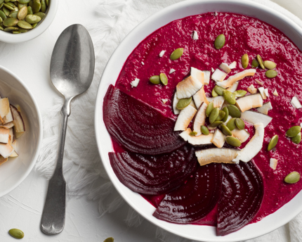 A bowl of red smoothie garnished with beet slices, seeds, and coconut