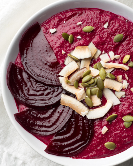 A bowl of red smoothie garnished with beet slices, seeds, and coconut