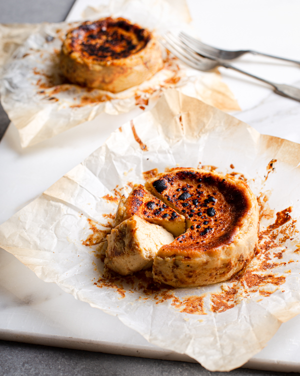 Two Basque cheesecakes on plates, one with two pieces cut out