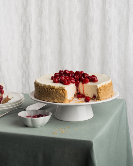 A cherry cheesecake with a slice missing on cake stand on a table