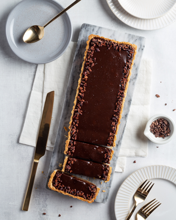 A chocolate chestnut ganache tart on a table with plates and cutlery