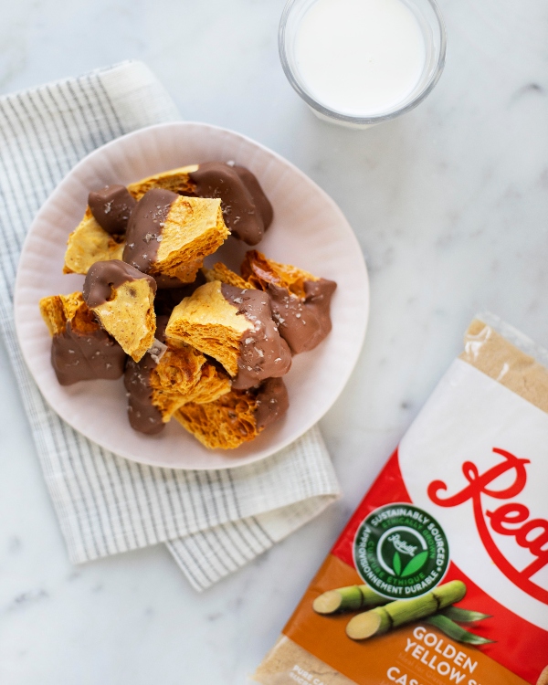 A bowl of chocolate coated sponge toffee on a striped towel with a bag of Redpath Golden Yellow Sugar