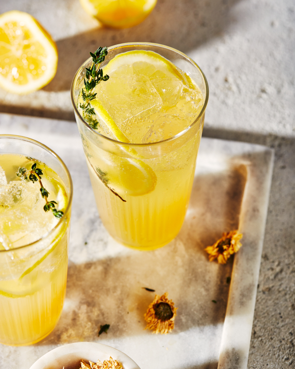 Two glasses of sparkling chrysanthemum tea lemonade on a marble tray, served with lemon slices and chrysanthemum sprigs and flowers