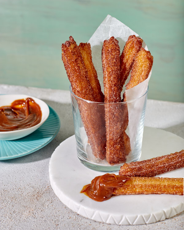   Churros with cinnamon sugar served in a glass with a bowl of dulce de leche