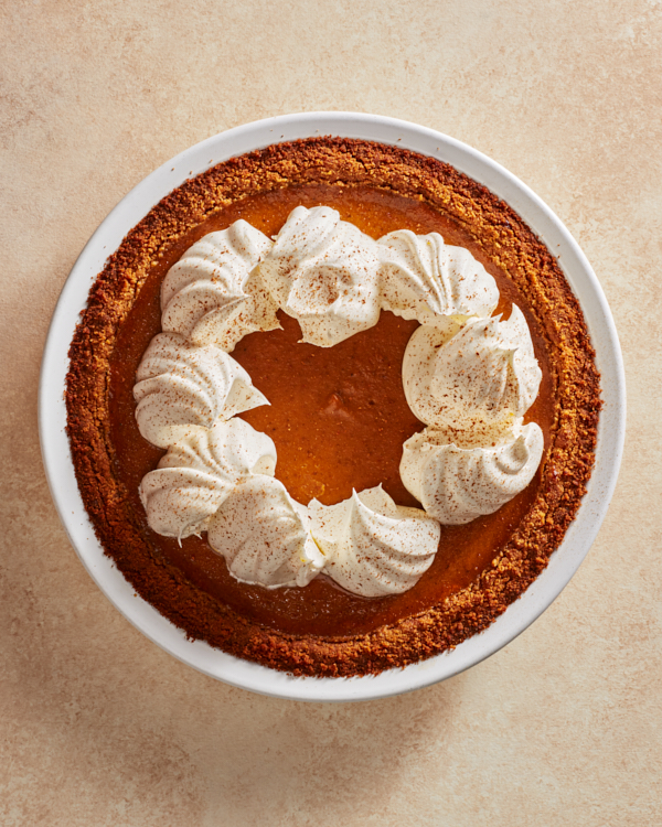 Whole pumpkin pie with whipped cream and ground cinnamon in a white pie plate.