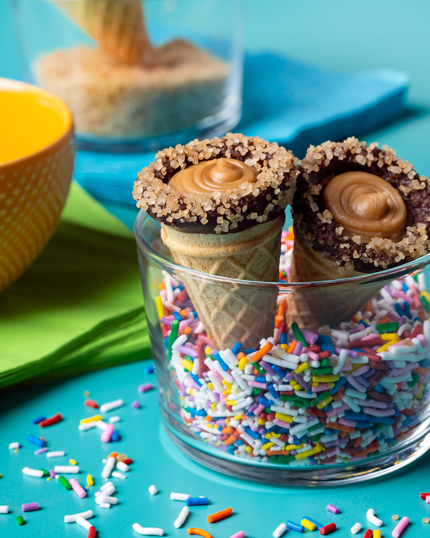 Chocolate dipped ice cream cones full of brown sugar fudge in a bowl of rainbow sprinkles