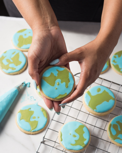 Hands lifting a butter cookie with blue and green icing from a wire cooling rack