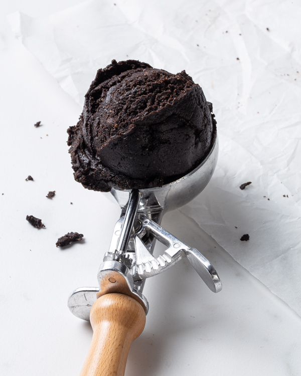 A scoop of edible dark chocolate cookie dough in an ice cream scooper