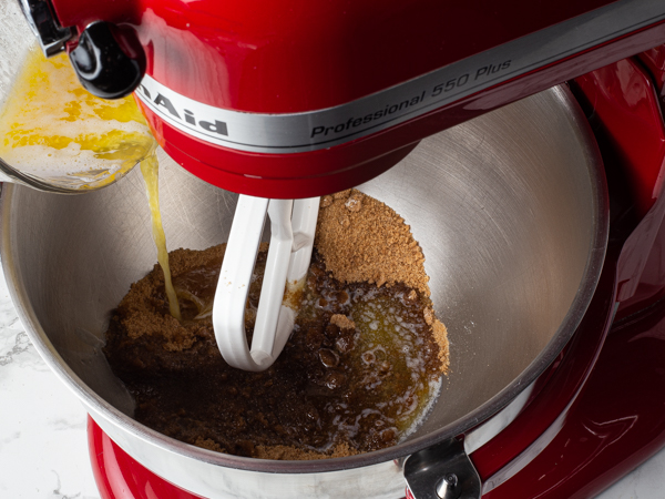 Pouring melted butter from a measuring cup into a stand mixer bowl of brown sugar