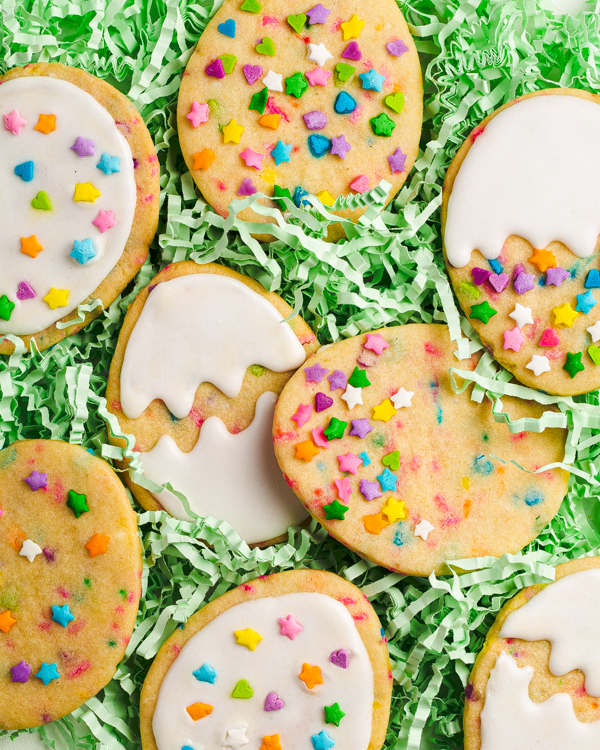 Easter egg cookies decorated with sprinkles and royal icing in a nest of edible green ribbons