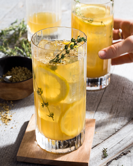 Two glasses of lemonade on ice with lemon slices and garnished with thyme