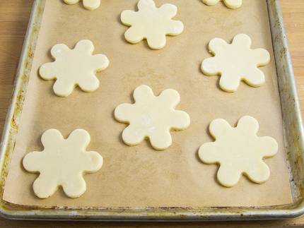 Uncooked flower shaped cookies on a baking sheet lined with parchment paper
