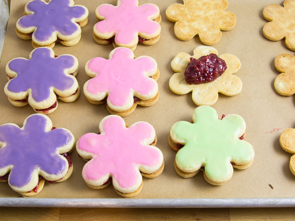 Flower shaped cookies on a baking sheet with colourful glaze and raspberry filling