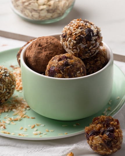 A green bowl full of fruit & nut energy bites resting on a matching plate