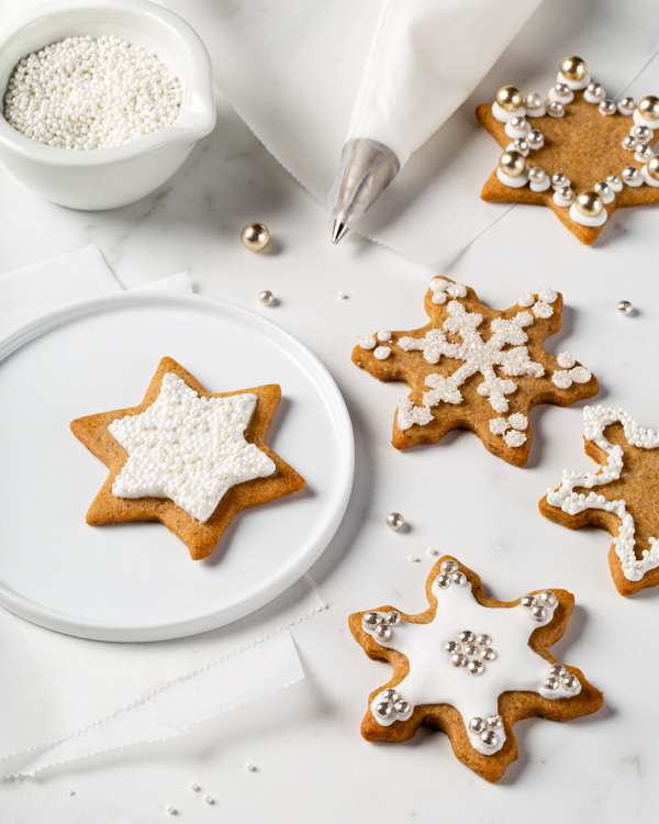 Gingerbread spiced sugar cookies decorated with royal icing, with a piping bag and a bowl of sprinkles