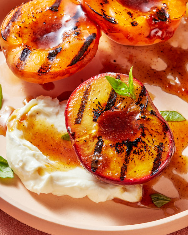 Three grilled peach halves with mascarpone and basil garnish and brown sugar glaze on a plate