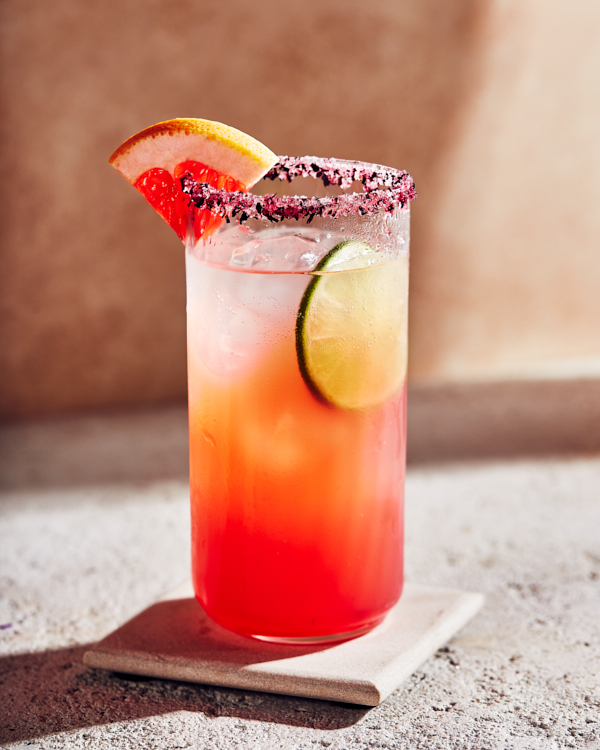 A glass of hibiscus paloma garnished with a wedge of grapefruit and rimmed with hibiscus petals.
