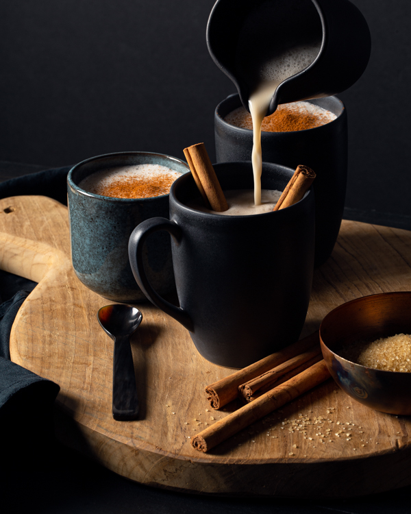 Pouring hot horchata from a pitcher into a mug with cinnamon sticks