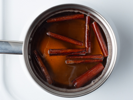 Melted turbinado sugar, water, and salt simmering in a pot with cinnamon sticks