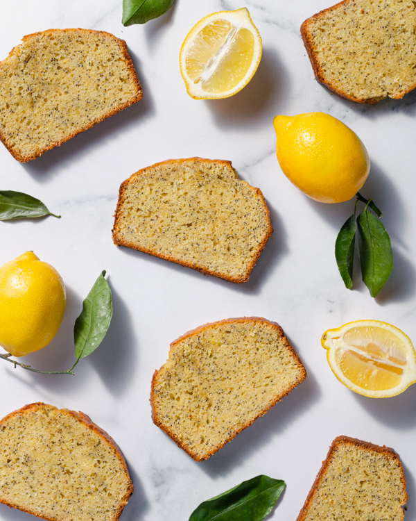 Slices of lemon poppy seed pound cake scattered on a marble counter with leaves and lemons