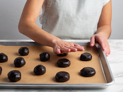 Flattening balls of dark chocolate cookie dough on a baking sheet by hand