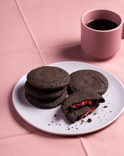 A plate of dark chocolate cookies stuffed with red marzipan shown with a cup of coffee