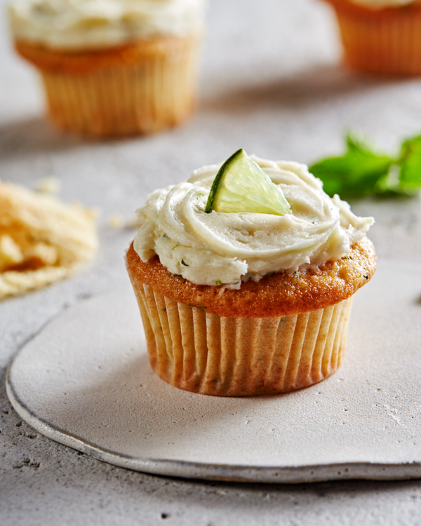 A mojito cupcake with ermine frosting on a plate, garnished with a lime wedge.