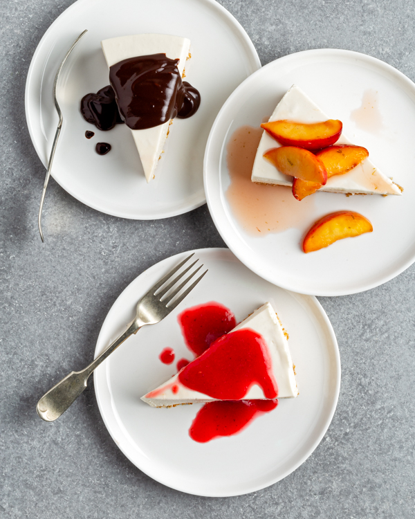 Three plated slices of No-bake vanilla cheesecake, one with peach topping, one with chocolate ganache, one with raspberry coulis.