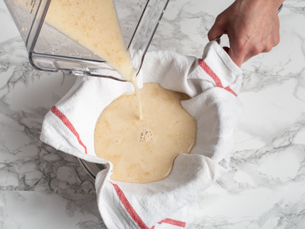 Straining blended oats and water in a bowl lined with a tea towel