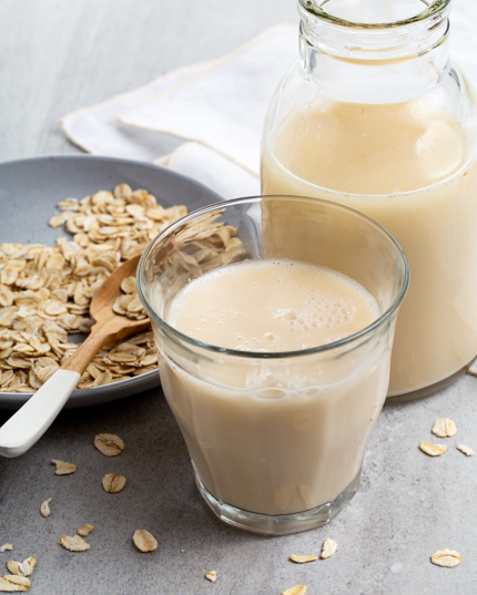 Vanilla oat beverage in a glass and a glass bottle with flaked oats on a plate