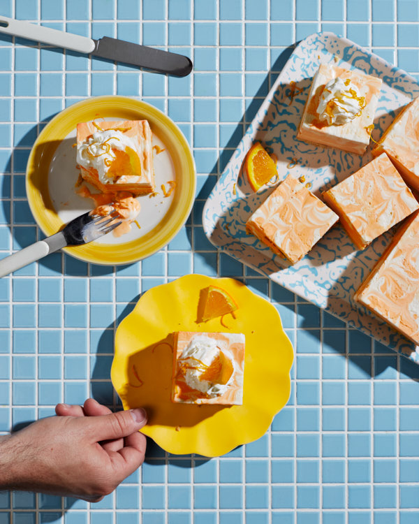 A piece of orange vanilla ice cream cake on a plate, garnished with whipped cream and an orange slice