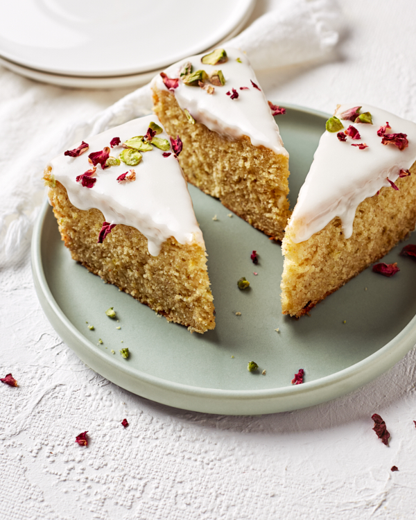 Three slices of Persian Love Cake with icing and rose petals on a pale green plate.