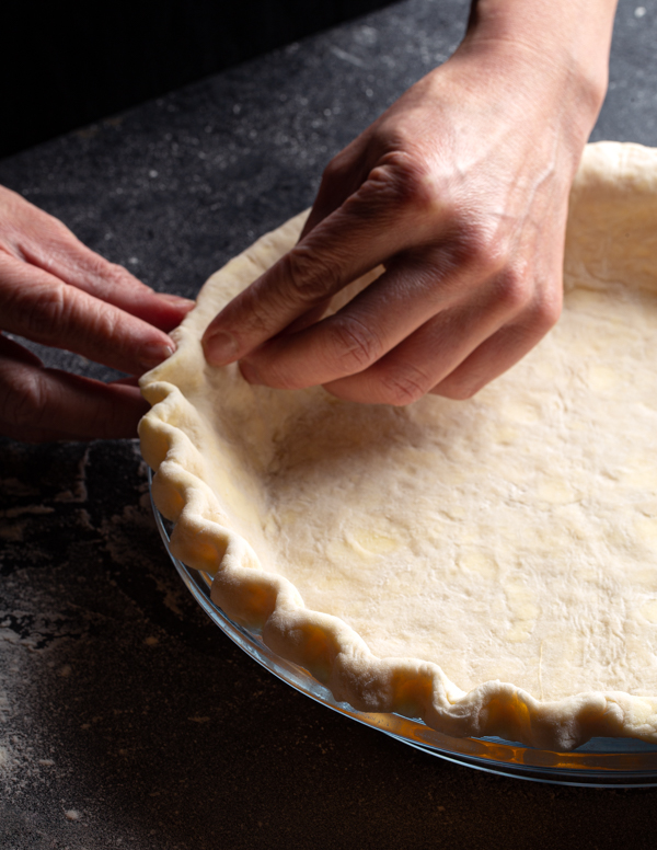 A pair of hands pinching the edge of a pie crust into scallops