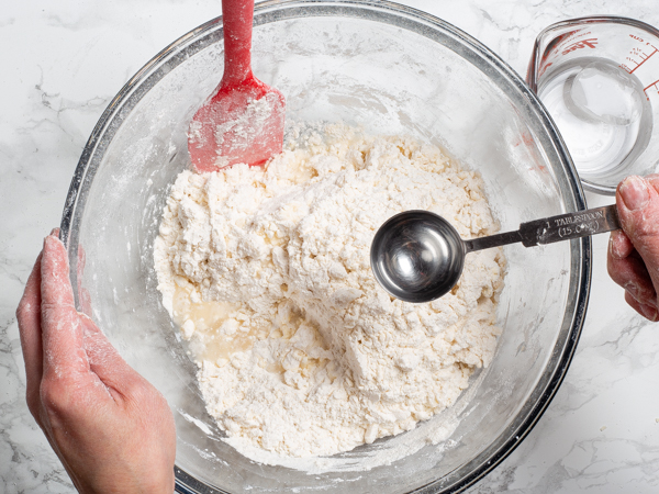 Sprinkling raw dough with ice water from a measuring spoon