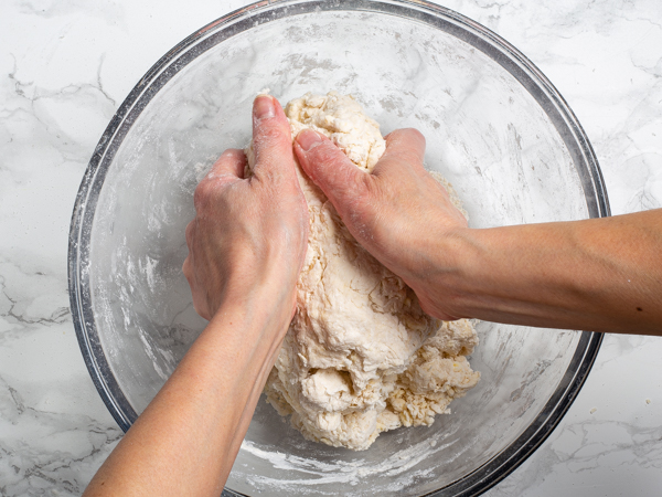 Working raw dough by hand in a large glass bowl